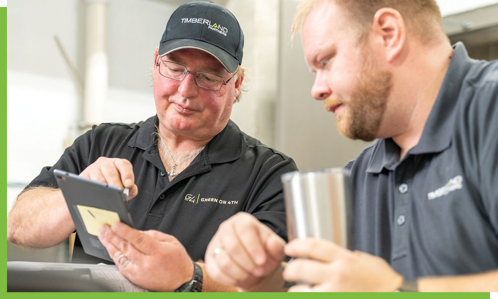Photo of a man showing another man something on a tablet.