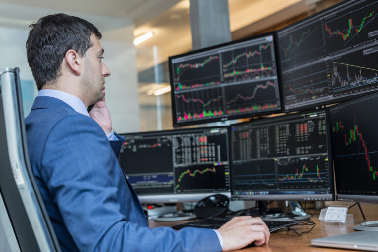 Stock broker trading online watching charts and data analyses on multiple computer screens